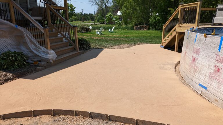 Tan colored stamped concrete patio with stone texture pattern in backyard