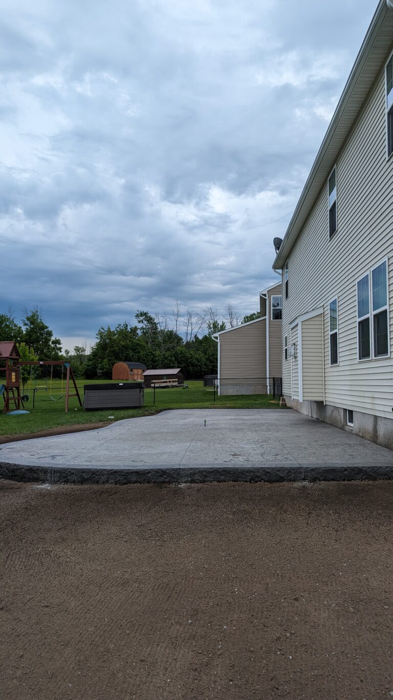 Large broomed concrete patio with curved edge behind residential home