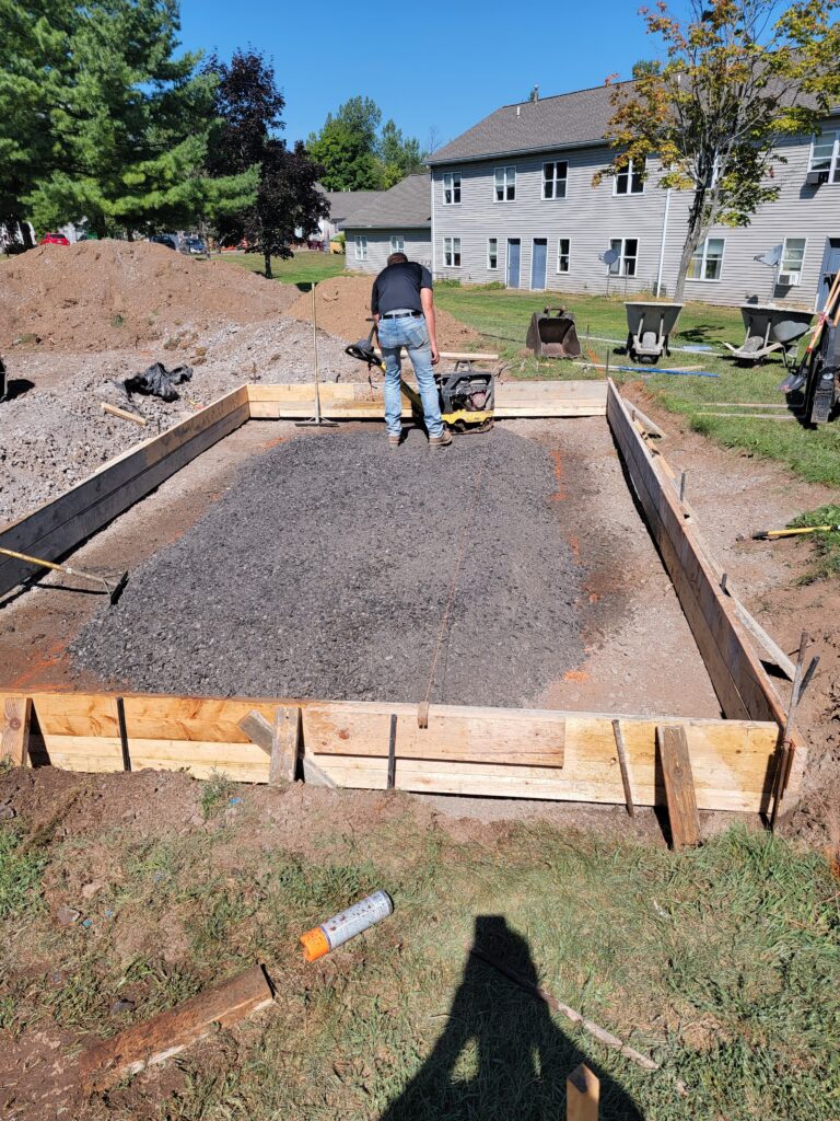 Worker compacting gravel sub-base in concrete forms for foundation