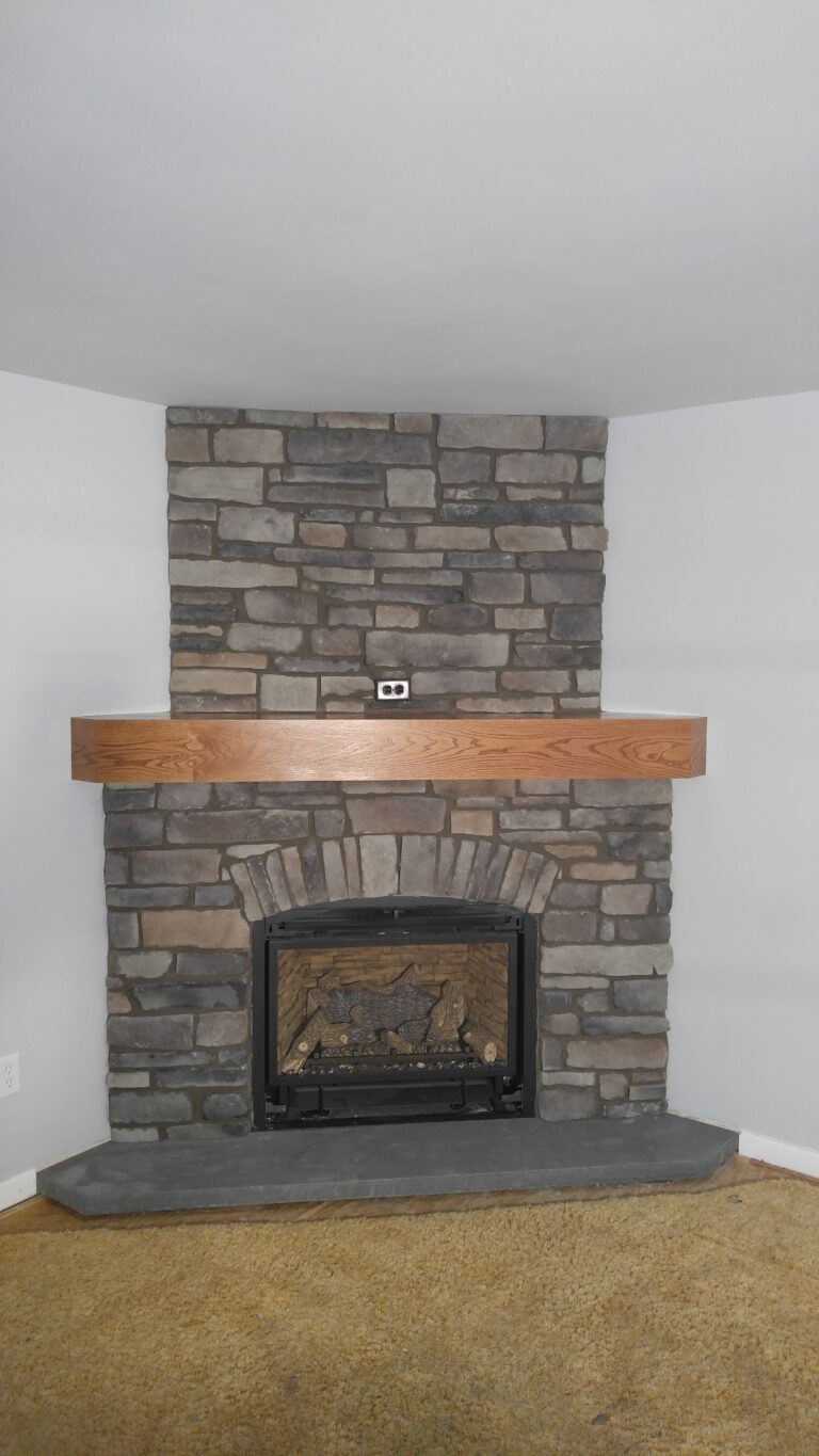 Ledgestone thin stone veneer fireplace surround with horizontal coursing in grey and brown tones, wood mantel shelf, Rochester NY