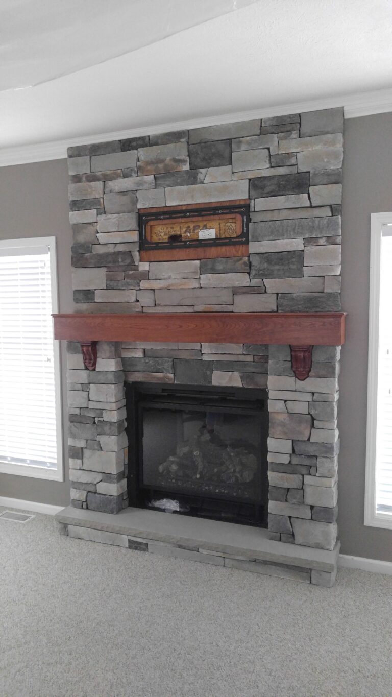 In-progress ledgestone stone veneer fireplace surround installation with grey horizontal coursing and wood mantel shelf, Rochester NY