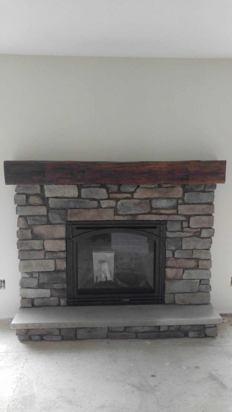 Stacked stone veneer fireplace surround with mixed grey and tan tones and rustic reclaimed wood beam mantel, Rochester NY