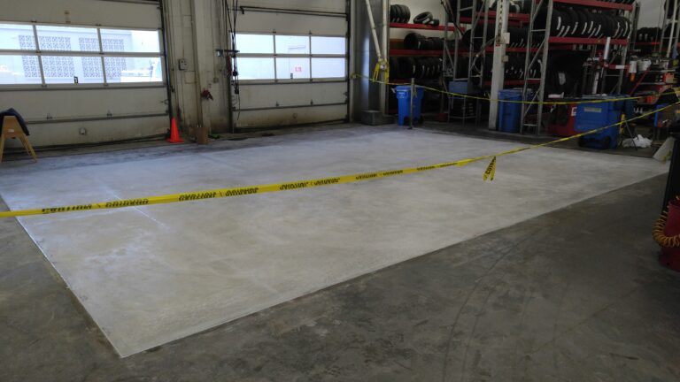 New concrete floor section poured inside a commercial auto shop in Rochester NY, cordoned off with caution tape while curing
