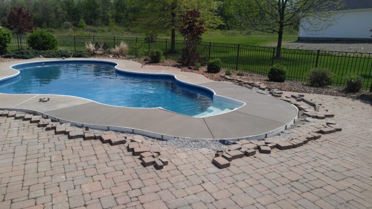 Smooth concrete pool deck surround around a kidney-shaped in-ground pool with black iron fence in Rochester NY