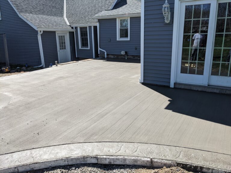 Wide broomed concrete rear patio with curved stamped concrete border installed in Penfield NY
