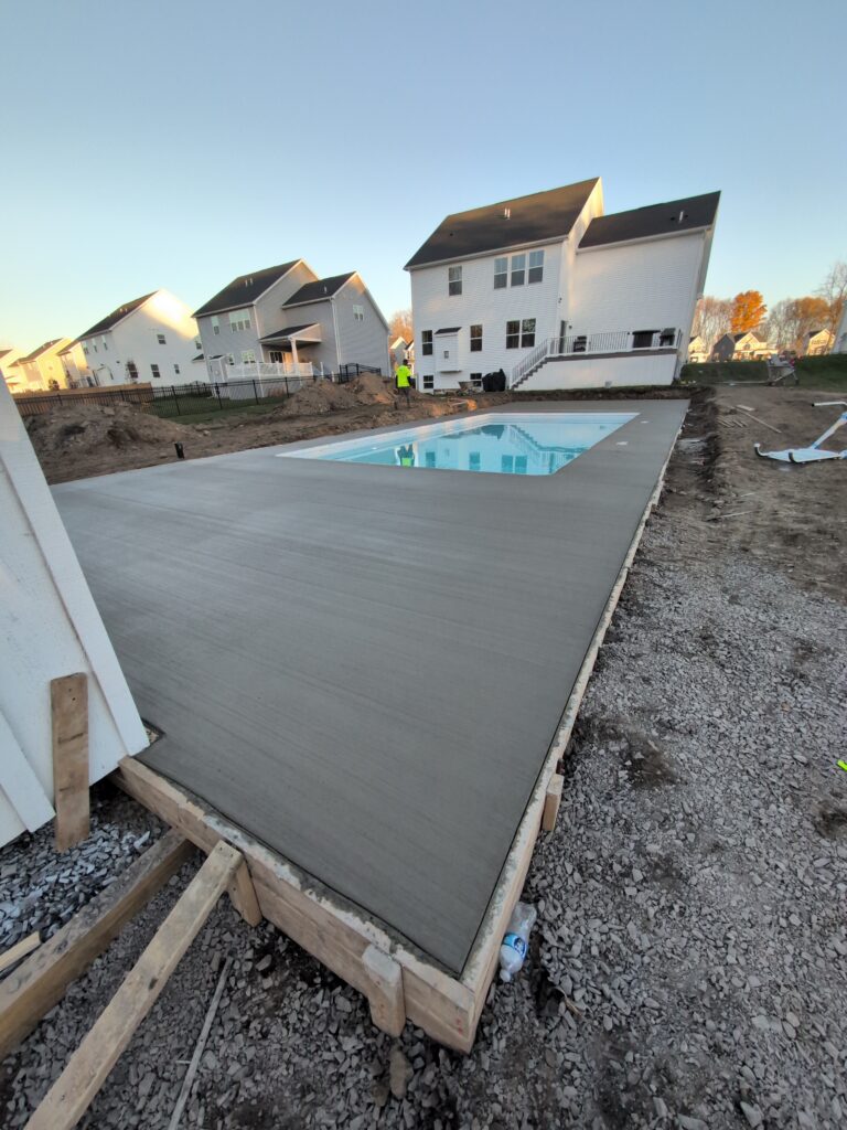 Fresh concrete pool deck slab being poured in wood forms at a new construction site in Fairport NY