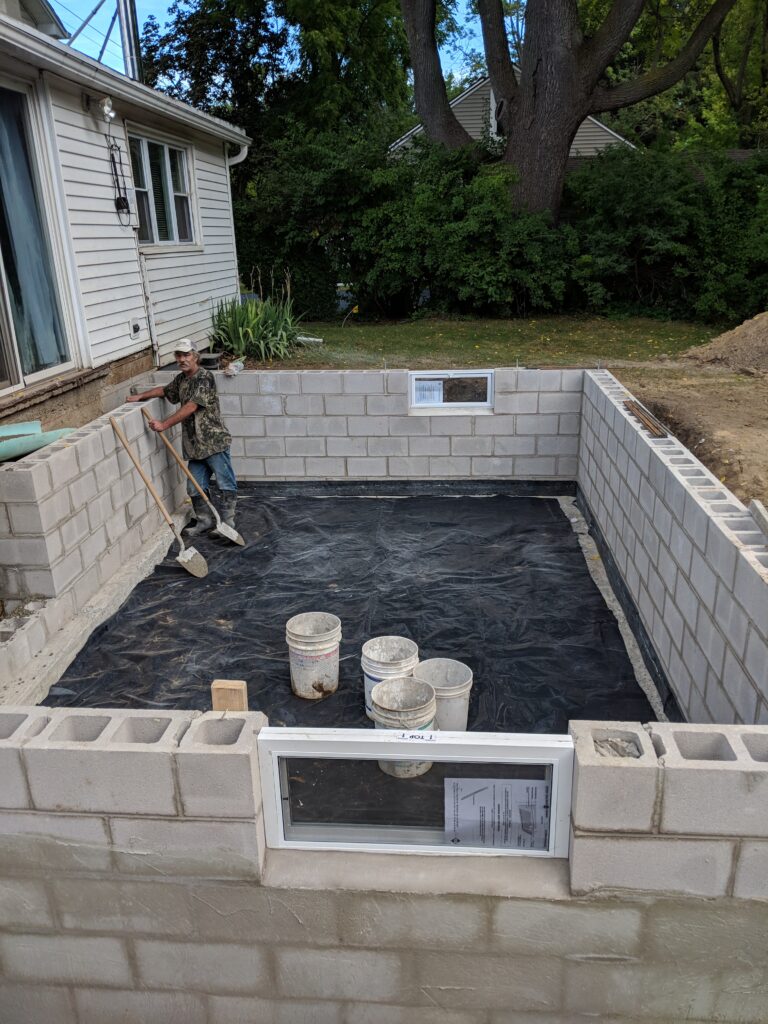 CMU block foundation walls under construction with vapor barrier floor and worker – Rochester NY residential foundation