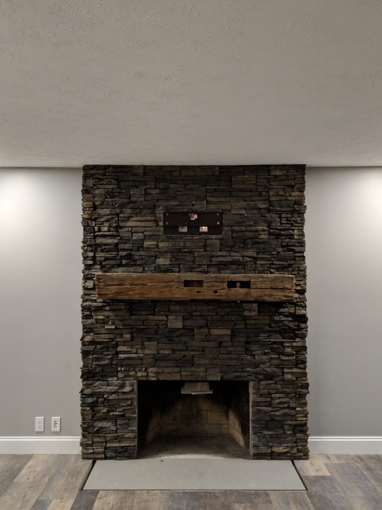 Front view of dark charcoal floor-to-ceiling ledgestone veneer fireplace surround with heavy wood beam mantel, Rochester NY
