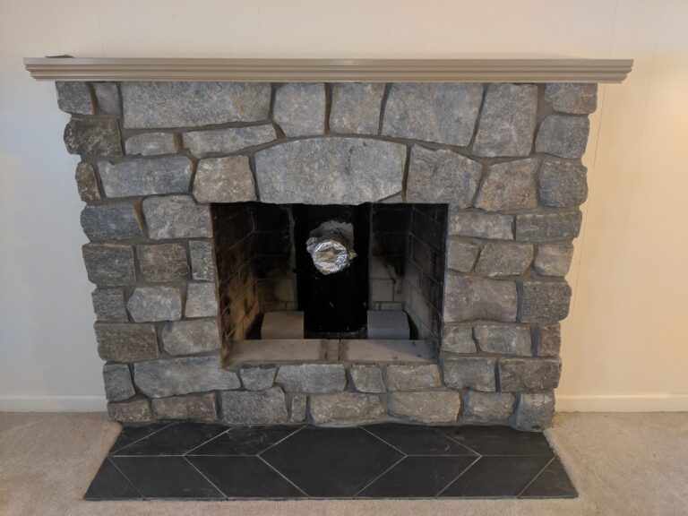 Natural stone fireplace surround with arched opening and dark bluestone tile hearth, Rochester NY interior
