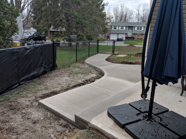 Newly poured curved broomed concrete side walkway along fence line connecting front yard to backyard patio, Rochester NY