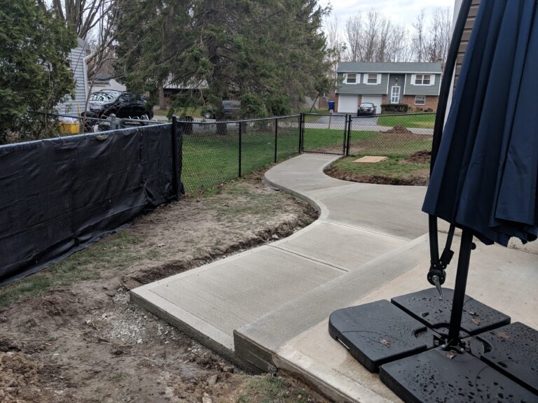New curved broomed concrete walkway running through a residential backyard near Rochester NY