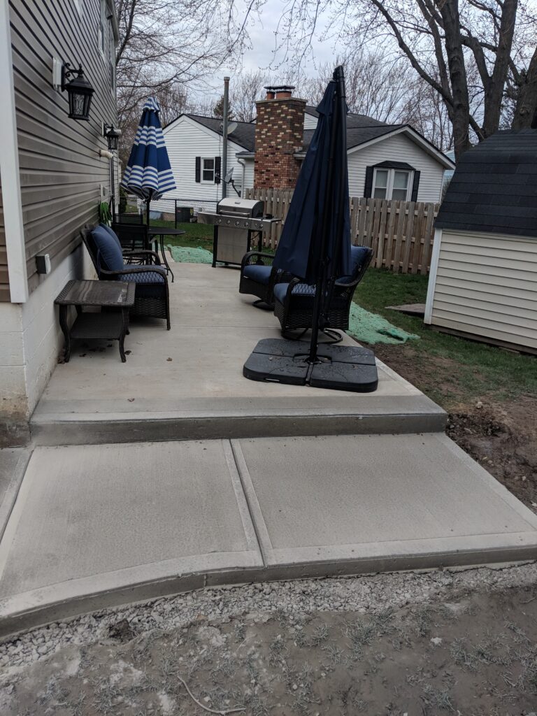 Broomed concrete backyard patio with outdoor furniture and step down to yard at Rochester NY home