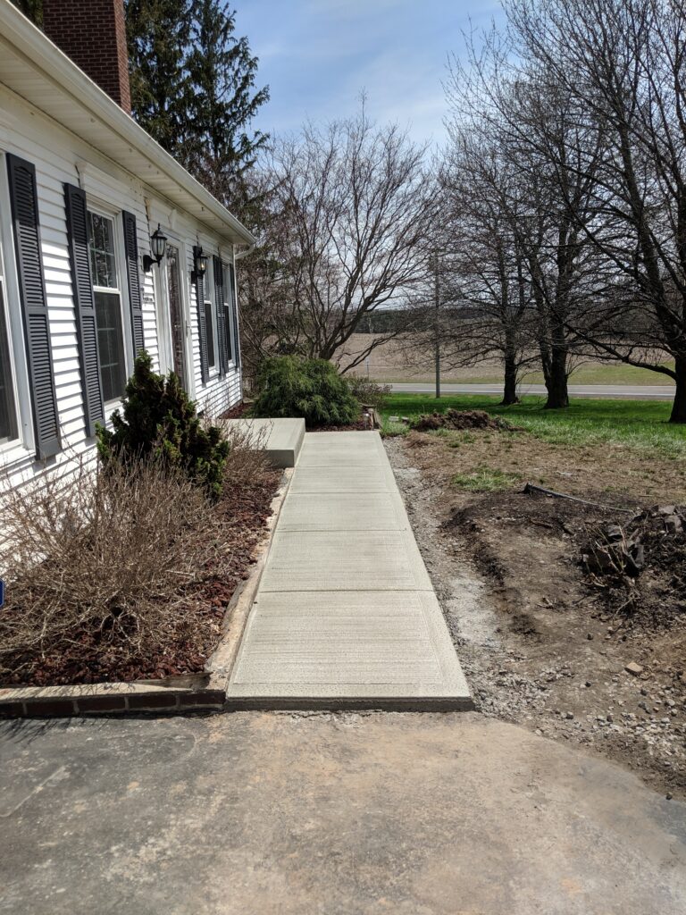 New broomed concrete front walkway running alongside a white colonial home in Monroe County NY