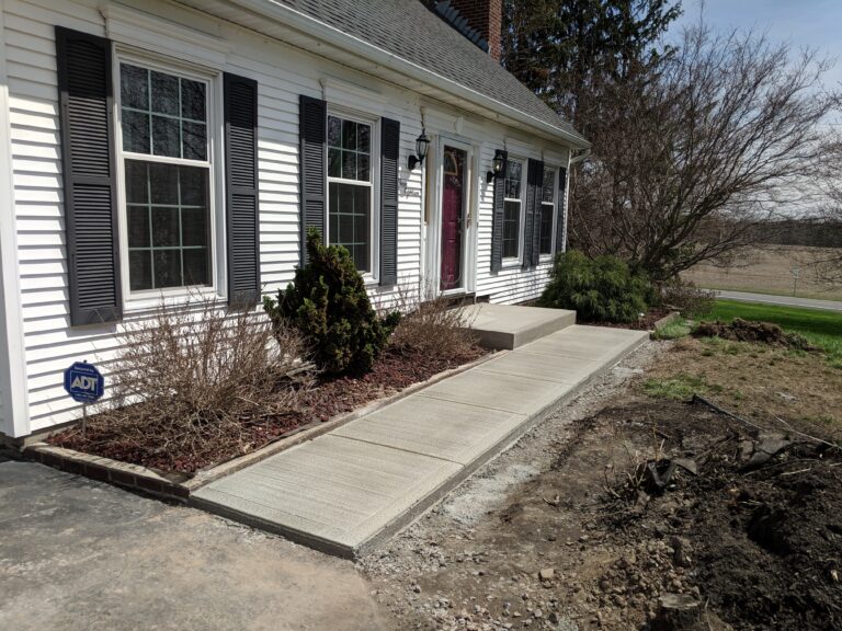 Wide-angle view of broomed concrete front walkway and entry steps at a colonial home in Monroe County NY
