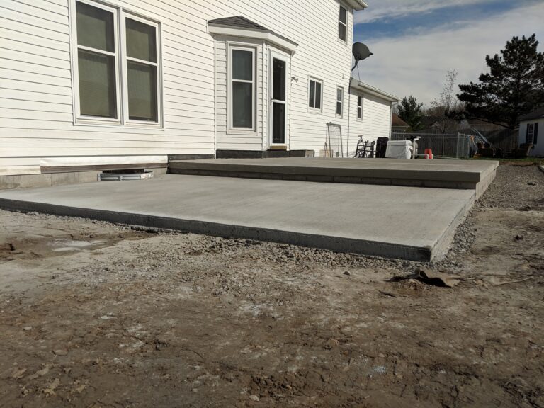 Elevated broomed concrete patio slab with bull-nose edges and a step down to gravel at a Rochester NY home