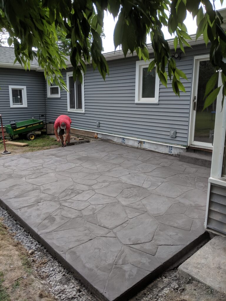 Angled view of large flagstone stamped concrete patio with crew and home in background – Rochester NY