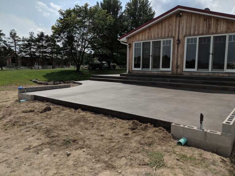 Large broomed concrete patio with wide steps at a rural Rochester NY property with cedar-sided building