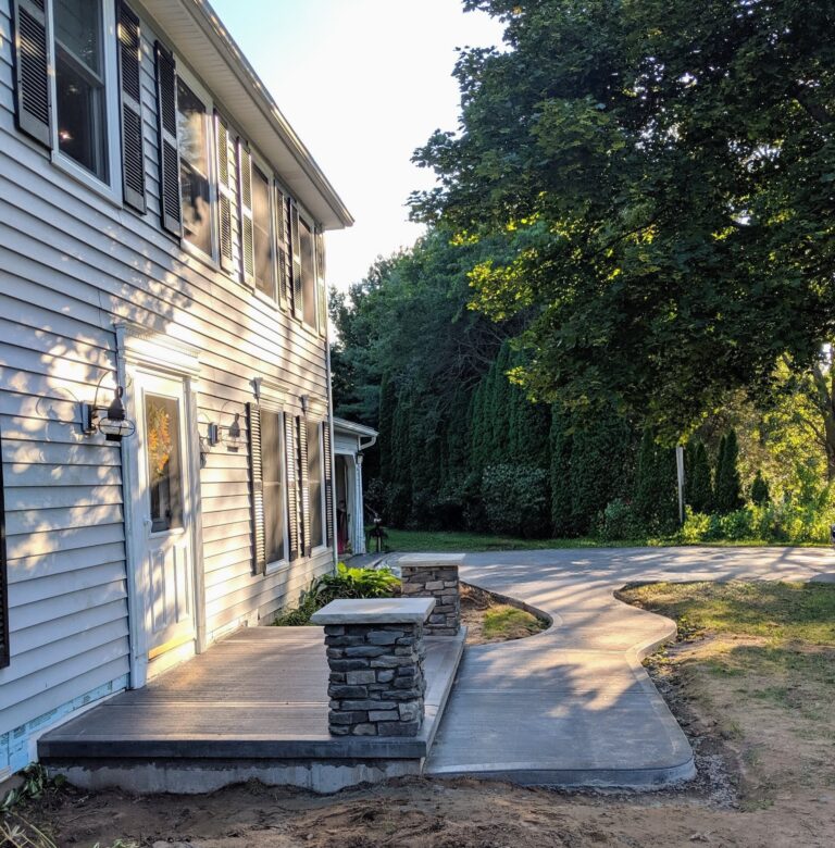 Wide concrete front walkway with stacked stone pillar landing at front entry photographed in evening light, Rochester NY