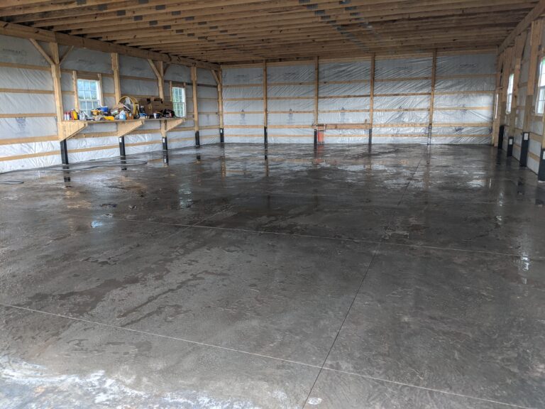 Large pole barn interior with freshly poured concrete floor featuring burn finish and control joints in Rochester NY