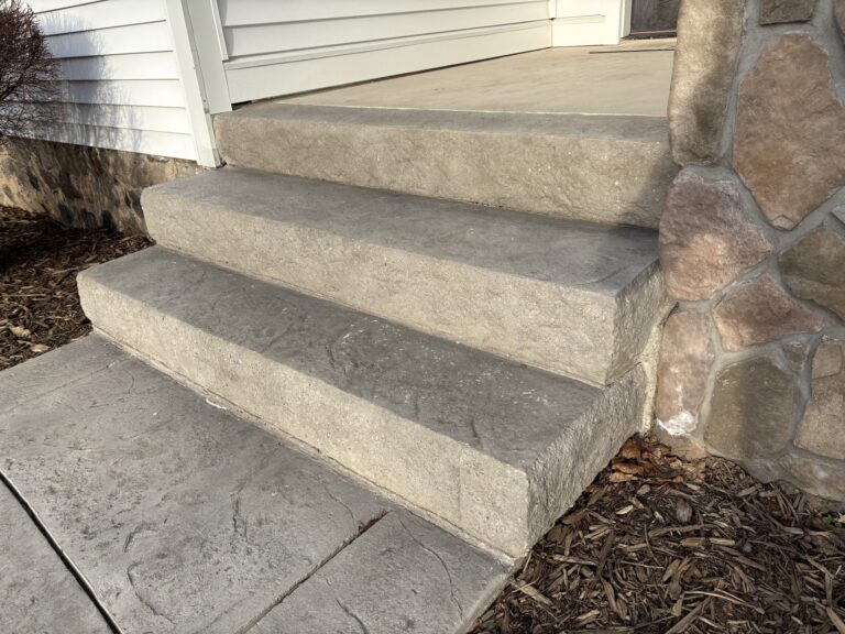 Stamped concrete entry steps with slate pattern texture beside fieldstone veneer column base