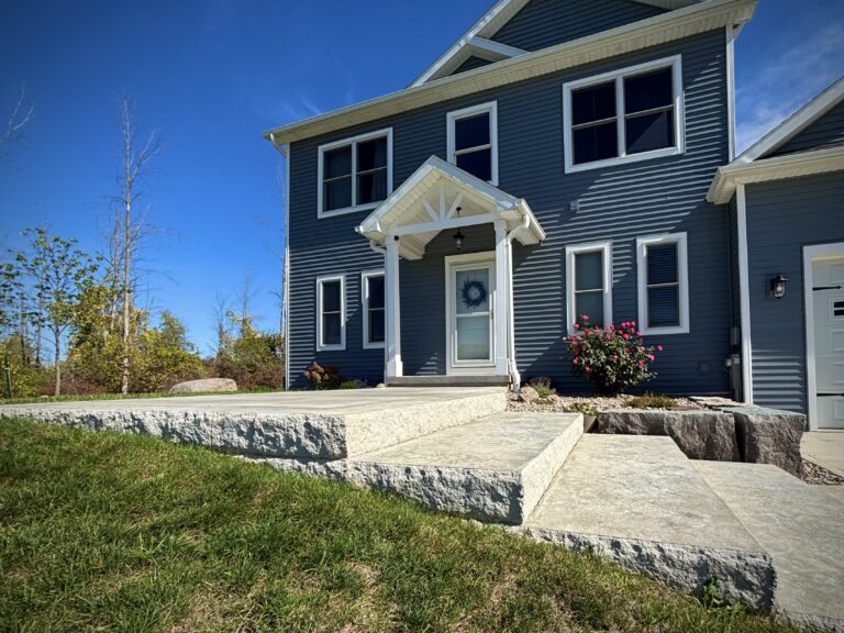 Wide natural stone slab steps with boulder retaining walls leading to front porch of blue new construction home