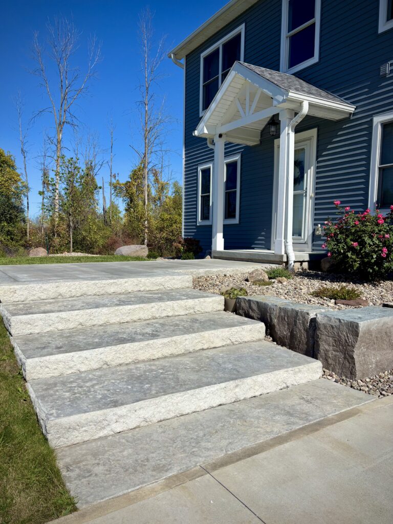 Angled view of natural stone slab steps with rough-cut boulder retaining wall at blue new construction home