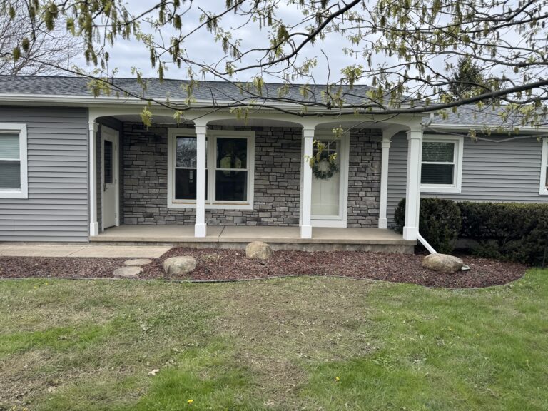 Grey ledgestone veneer covering front porch facade of ranch home with white columns and boulder landscaping