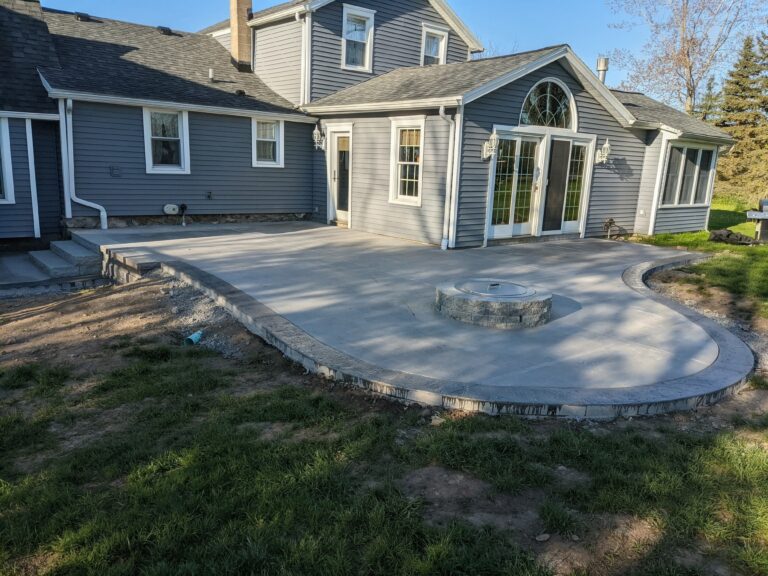 Large concrete patio with natural stone fire pit and curved stone edging behind suburban home, Rochester NY