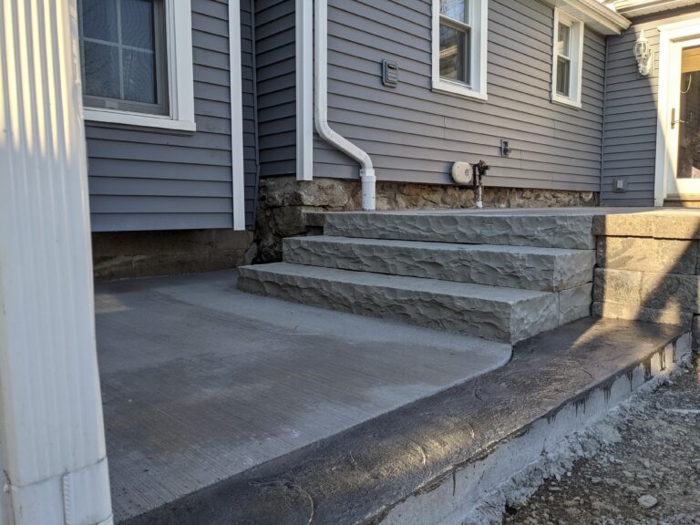 Side view of natural stone tile patio with boulder seat wall and concrete border, Monroe County NY