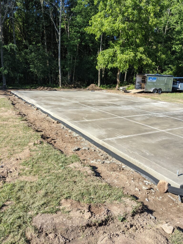 Newly poured large broomed concrete slab with expansion joints next to a wooded lot in the Rochester NY area