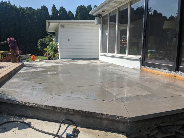 Wide-angle view of completed natural stone tile patio with raised stone-capped planting bed, Rochester NY