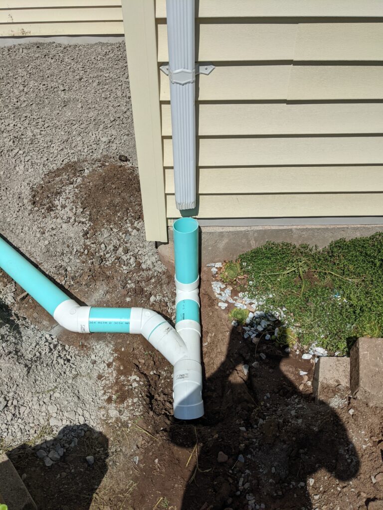 PVC downspout drainage pipe connection with wye fitting buried at a home foundation – Rochester NY