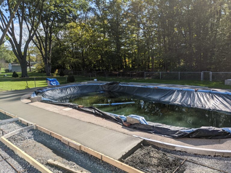 Concrete pool deck installation showing rebar reinforcement grid and partially poured sections around a covered in-ground pool
