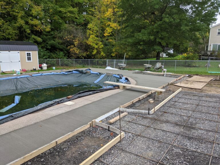 Freshly poured and finished broomed concrete pool deck surround around a covered in-ground pool, ready to cure