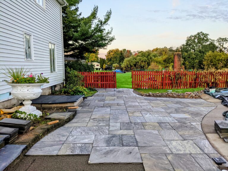 Large natural stone tile patio in charcoal grey beside white home with open countryside, Rochester NY
