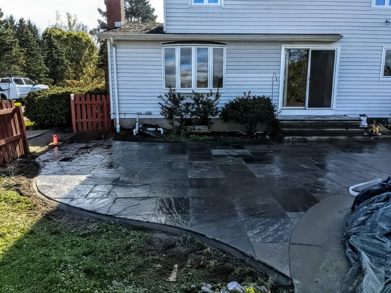 Completed natural stone tile patio and pool surround curving around in-ground pool, Rochester NY backyard