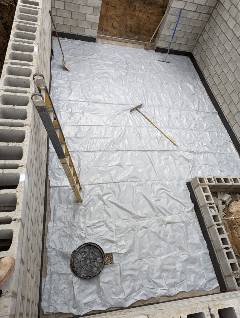 Polyethylene vapor barrier laid inside CMU block foundation walls before concrete slab pour – Rochester NY