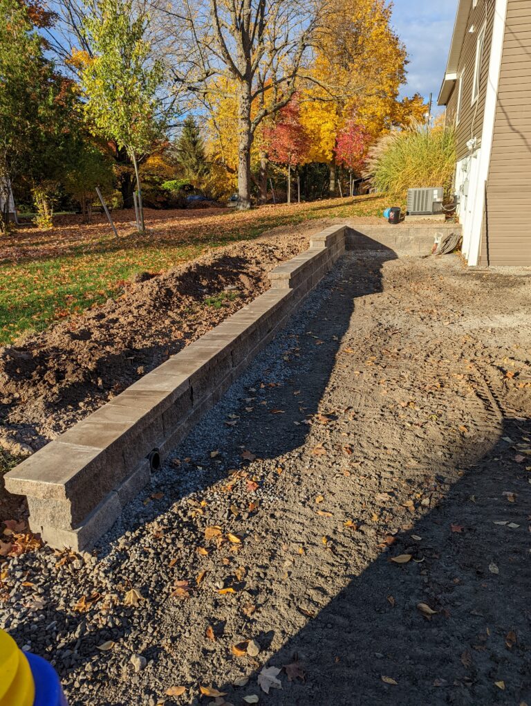 Newly installed concrete block retaining wall along gravel driveway with fall foliage, Rochester NY