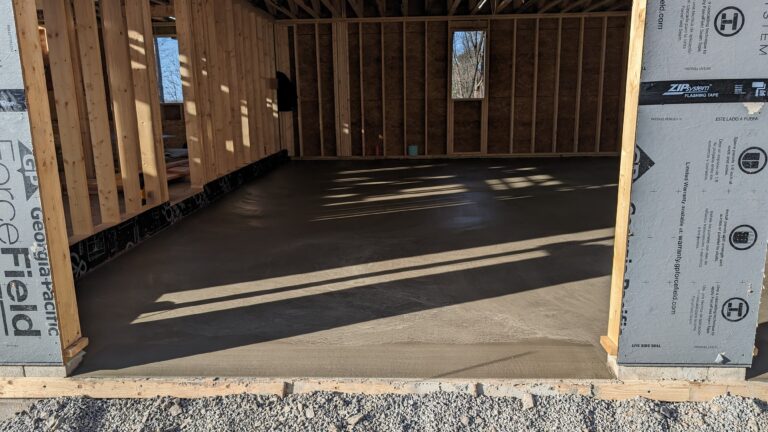 Freshly poured concrete garage floor inside new construction wood-framed garage with ZIP sheathing in Rochester NY
