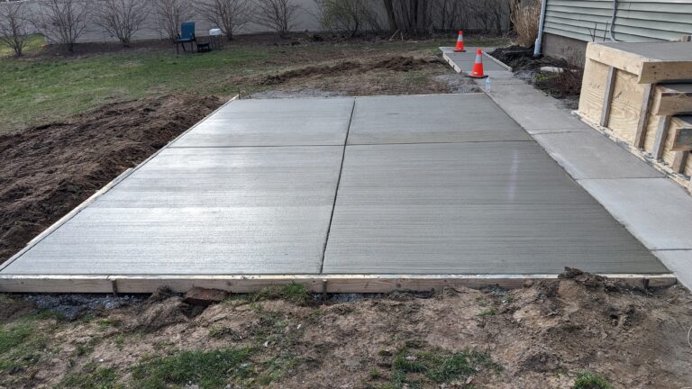 Freshly poured broomed concrete backyard patio with safety cones and control joints at a Rochester NY home