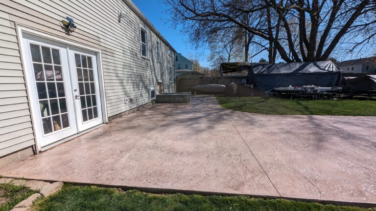 Side view of stamped concrete patio in pink-tan flagstone pattern with French doors – Rochester NY