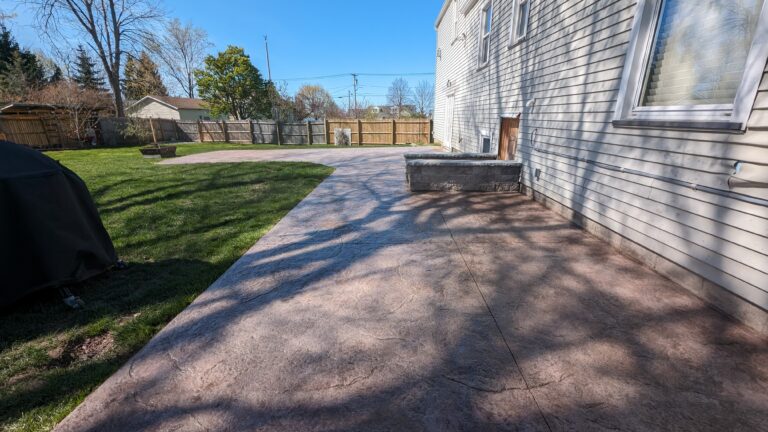 Stamped concrete backyard patio with raised step and slate texture along home exterior – Rochester NY