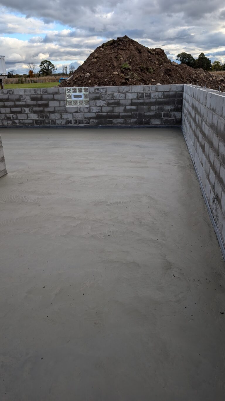 Freshly poured and power-troweled concrete basement floor slab inside CMU block foundation walls – Rochester NY