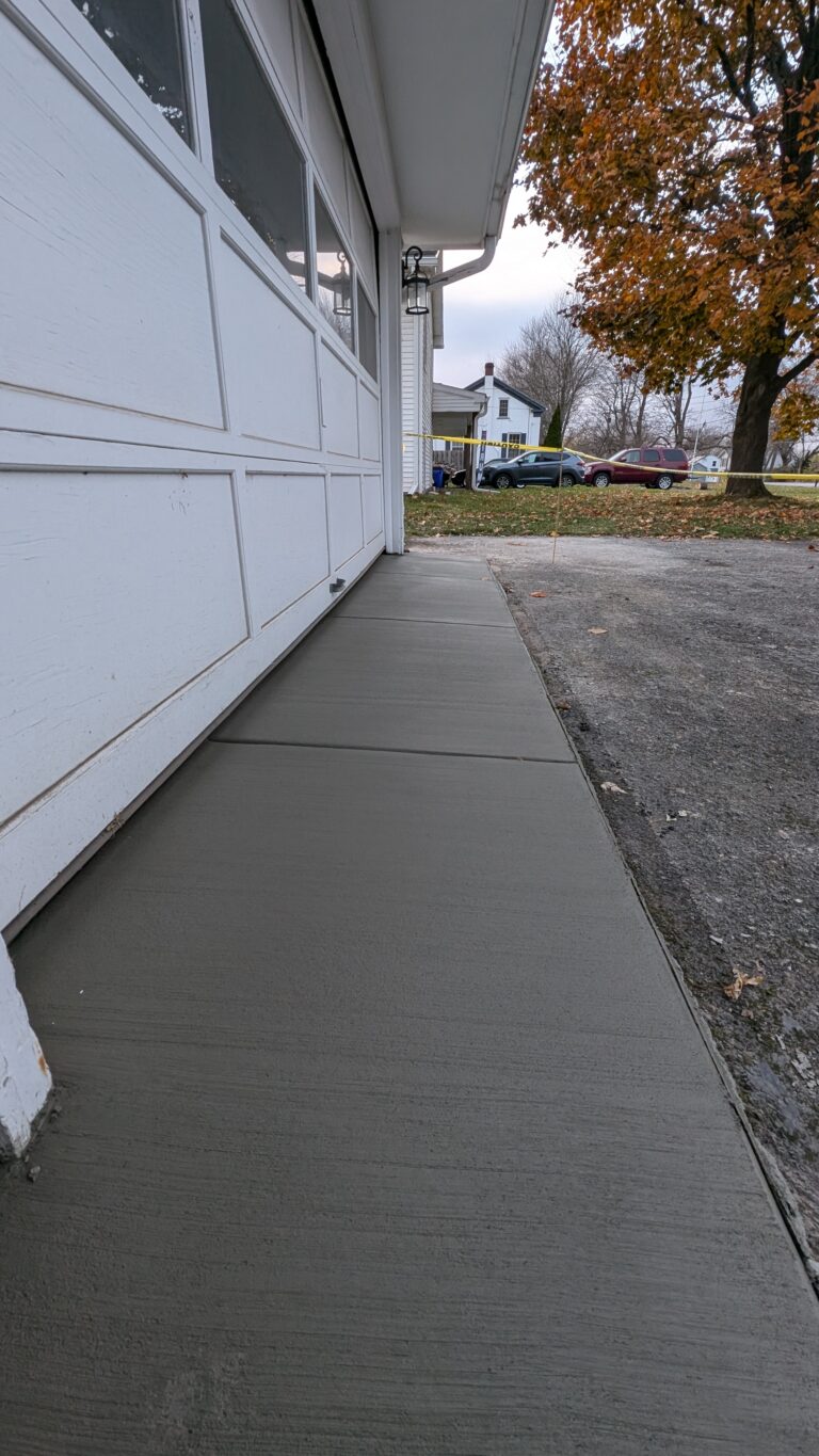 Freshly poured broom-finished concrete sidewalk along white residential garage in autumn in Rochester NY
