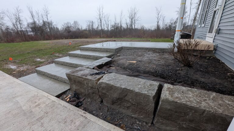 Natural stone entry steps with rough risers and large boulder accent planting at new construction, Rochester NY