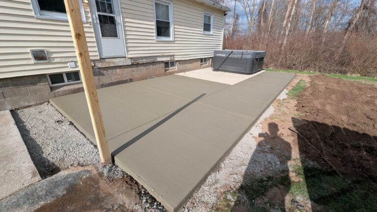 Wide view of new broomed concrete patio with hot tub and connecting walkway at a Rochester NY home