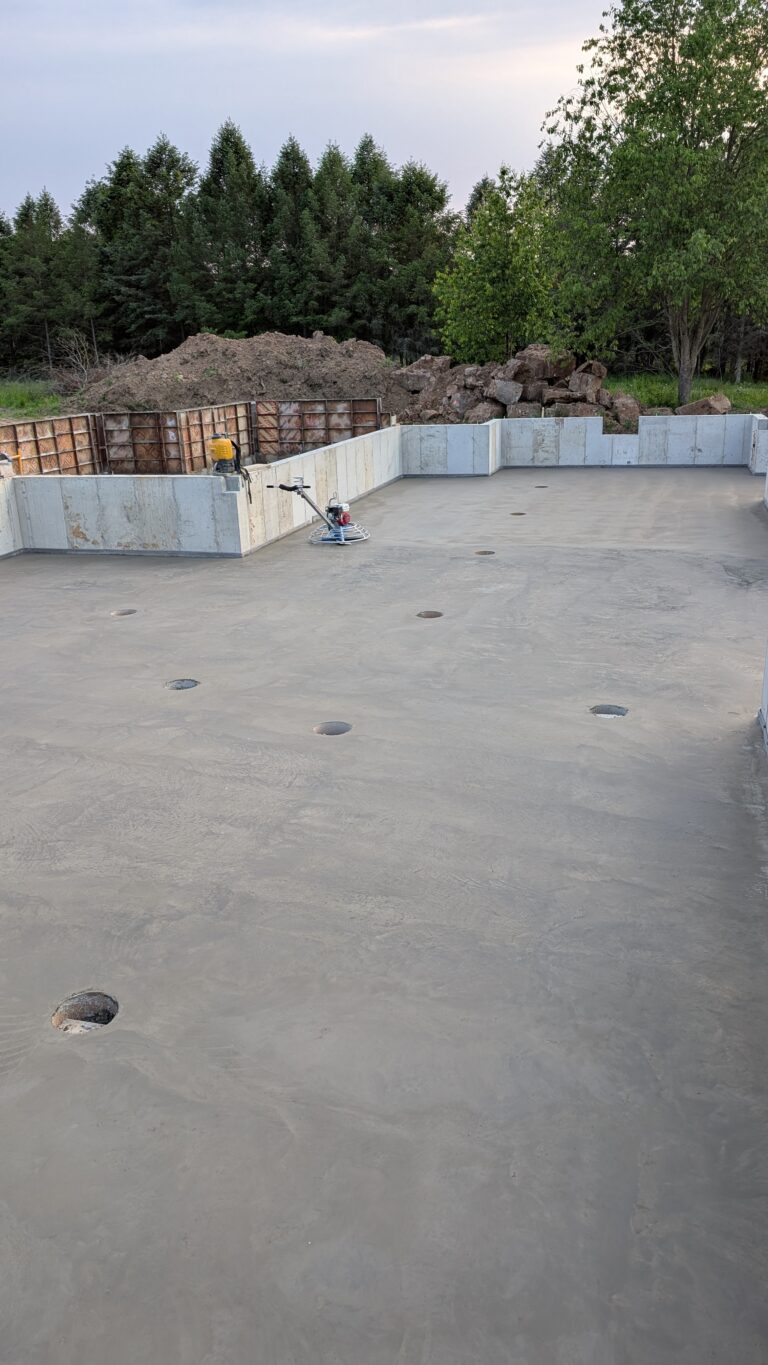 Power trowel finishing freshly poured concrete basement floor slab at dusk inside poured foundation walls – Rochester NY