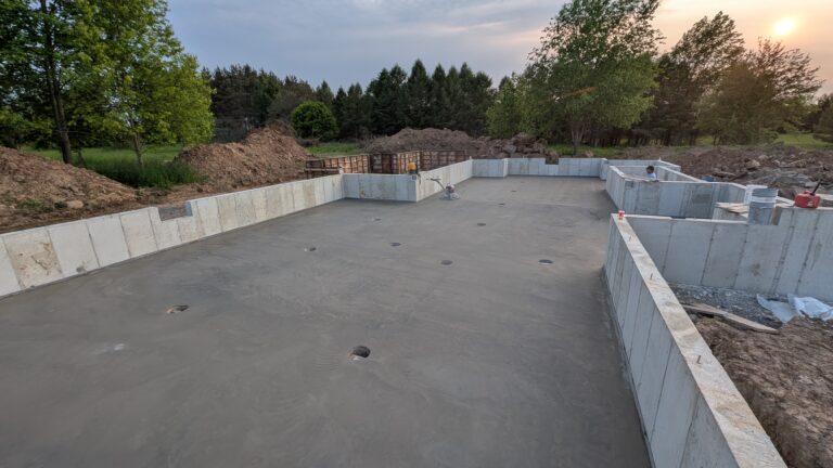 Wide view of freshly poured and troweled concrete basement slab inside poured foundation walls at sunset – Rochester NY