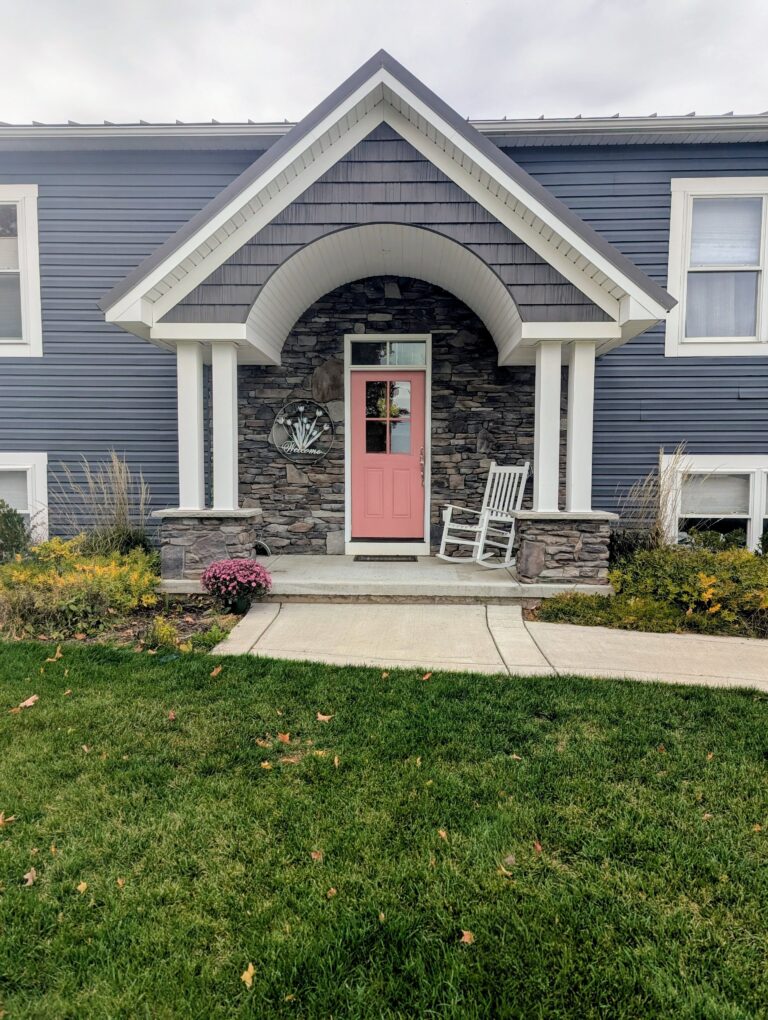 Dark grey ledgestone veneer on front entry portico with arched gable and coral door on blue-sided home