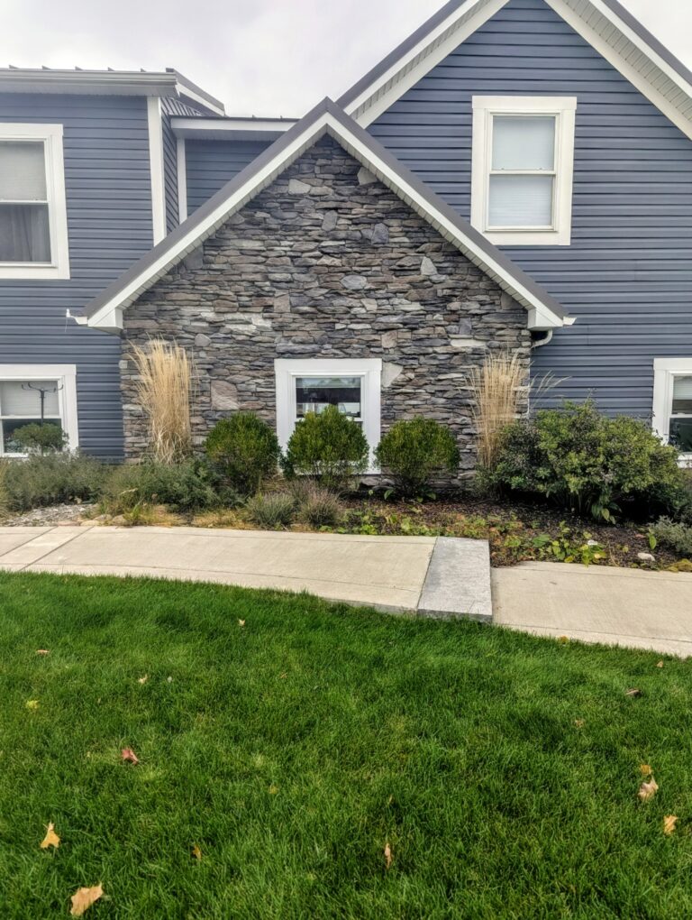 Full-height dark grey ledgestone veneer on accent gable wall of blue-sided home with centered window